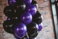 A colorful array of purple and black balloons hangs in an eye-catching display from a sturdy brick wall, Gothic black and purple