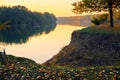 Colorful autumn forest landscape at sunset, trees near river and sky, bright sunlight reflected in water Royalty Free Stock Photo