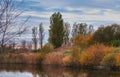 Colorful autumn forest trees by a river. Beautiful nature landscape of a lake with calm water near lush tree foliage and Royalty Free Stock Photo