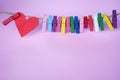 Red heart and colorful paper clips on rope on soft pink purple background.