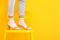 Legs of young woman in socks and sandals standing on chair against color background Royalty Free Stock Photo