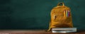 The colorful backpack resting on a stack of books on a wooden desk. AI generated image Royalty Free Stock Photo