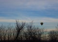 Colorful ballon with basket flying above trees silhouettes against morning sky as winter fun background. Winter aerial sport.