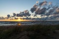 Colorful beach sunset with the sun dropping into the ocean under an expressive sky and marsh grass in sand dunes Royalty Free Stock Photo