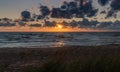 Colorful beach sunset with the sun dropping into the ocean under an expressive sky and marsh grass in sand dunes Royalty Free Stock Photo