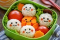 A colorful bento box featuring rice balls with smiling faces and assorted vegetables Royalty Free Stock Photo