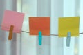 Colorful blank sticky notes hanging on natural wooden rope in pink, orange and yellow colors. Royalty Free Stock Photo