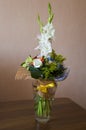 Colorful bouquet with such flowers as gladiolus, orchid, roses, callas, mimosa are standing in the big glasses vase. Tints of whit Royalty Free Stock Photo