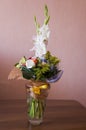 Colorful bouquet with such flowers as gladiolus, orchid, roses, callas, mimosa are standing in the big glasses vase. Tints of whit Royalty Free Stock Photo