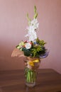 Colorful bouquet with such flowers as gladiolus, orchid, roses, callas, mimosa are standing in the big glasses vase. Tints of whit Royalty Free Stock Photo