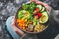 Colorful bowl with avocado and vegetables in a woman& x27;s hands