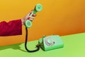 Colorful bright image of female hand holding old-fashioned green colored phone, picking up handset isolated over orange Royalty Free Stock Photo