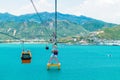 Colorful cabins of funicular over the sea with green mountains in the background and sandy shore Royalty Free Stock Photo