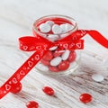 Colorful candy jar decorated with a red bow with hearts on white wooden background. Valentines day concept Royalty Free Stock Photo