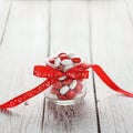 Colorful candy jar decorated with a red bow with hearts on white wooden background. Valentines day concept Royalty Free Stock Photo