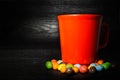 Colorful candy surround of red cup on black wooden texture background