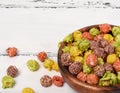 Colorful caramel popcorn in a wooden bowl on a white wooden back