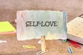 A colorful card with the words self love is displayed on a creative workspace. Surrounding elements include paper clips Royalty Free Stock Photo