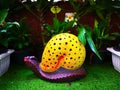 The colorful ceramic snail with yellow shell and purple body, which is on green artificial grass and decorated in a public small Royalty Free Stock Photo