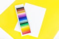 Colorful chalk pastels in box and sheet of white paper with space for text on yellow background Royalty Free Stock Photo