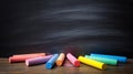 Colorful chalk sticks scattered on a rustic wooden surface below a dark blackboard. Royalty Free Stock Photo