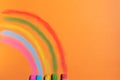 Colorful chalks drawing a rainbow on a orange background