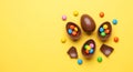 Colorful chocolate Easter eggs are displayed with candy inside and scattered around on a vibrant yellow background Royalty Free Stock Photo