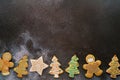 Colorful Christmas glazed cookies lie along the bottom edge on a black shabby background