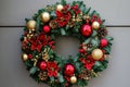 A colorful Christmas wreath adorned with ornaments and a bow is hanging on a bright red door, A traditional Christmas wreath with Royalty Free Stock Photo