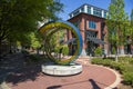 A colorful circular glass sculpture at the Waterhouse Pavilion with red brick buildings and sidewalks, lush green trees and plants