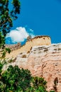 Colorful cliff walls in the high desert of New Mexico with a blue sky and green trees