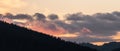 Colorful clouds at sunset pass over a hill covered with trees Royalty Free Stock Photo