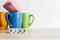 Colorful coffee mugs with a word `Kids` on white background on table