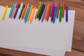 Colorful crayons with a white blank sheet of paper on a wooden b