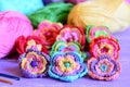 Colorful crochet flowers collection. Crochet flowers, multicolored cotton yarn, crochet hooks on purple wooden table