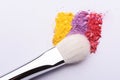 Colorful crumbled eye shadow powder and makeup brush on a white background