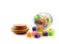 Colorful cube jelly candies spilling out of vacuum glass bottle with wooden lid fell to the ground isolated on white background Royalty Free Stock Photo