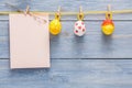 Colorful Decorative Eggs Hanging on Yellow String Above Blank Note on Wooden Background Royalty Free Stock Photo