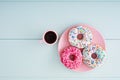 Colorful donuts in a pink plate with pink cappuccino coffee cup on a pastel blue wooden table background Royalty Free Stock Photo