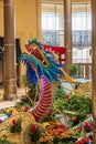 A colorful dragon sculpture surrounded by large gold coin, colorful flowers and lush green plants at The Venetian Resort and Hotel