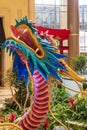 A colorful dragon sculpture surrounded by large gold coin, colorful flowers and lush green plants at The Venetian Resort and Hotel