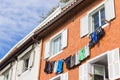 Colorful drying clothes against house facade. Traditional building exterior with window shutters, clothesline and grass on roof.