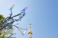 Colorful easter birds on tree branches against the blue spring sky and church cross background.