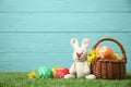 Colorful Easter eggs, basket and bunny toy on grass against light blue wooden background Royalty Free Stock Photo