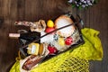 Colorful easter eggs in a basket with cake, red wine, hamon or jerky and dry smoked sausage on wooden background.