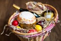 Colorful easter eggs in a basket with cake, red wine, hamon or jerky and dry smoked sausage on wooden background. Royalty Free Stock Photo