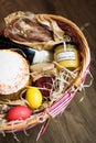 Colorful easter eggs in a basket with cake, red wine, hamon or jerky and dry smoked sausage on wooden background. Royalty Free Stock Photo