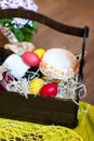 Colorful easter eggs in a basket with cake, red wine, hamon or jerky and dry smoked sausage on wooden background. Royalty Free Stock Photo