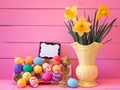 Colorful Easter Eggs in Carton with Vintage Yellow Vase filled with Spring Daffodils against Bright Pink Wood Board Background wit Royalty Free Stock Photo