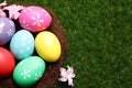 Colorful Easter eggs in decorative nest on green grass, top view. Space for text Royalty Free Stock Photo